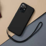 Smartphone posé sur une table avec coque noire et dragonne détachée, illustrant une chute évitée grâce à un accessoire de maintien.