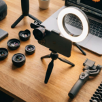 Kit complet d'accessoires photo smartphone comprenant un trépied, une ring light, des objectifs additionnels et un stabilisateur gimbal sur un bureau en bois.